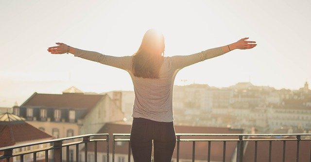 朝、バルコニーで気持ちよさそうに両手を広げる女性